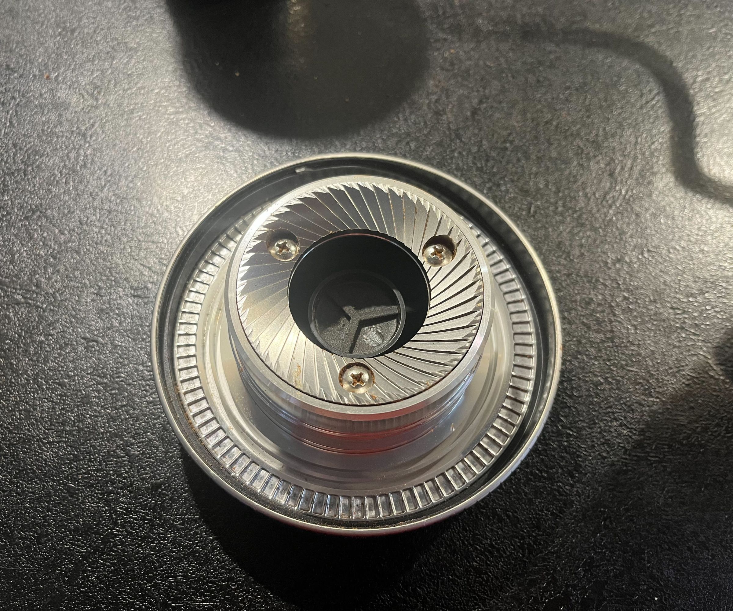 A stainless steel coffee grinder burr on a black counter. 