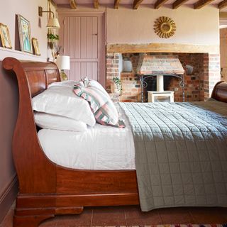 wooden sleigh bed in guest bedroom with white wood burning stove, pink walls and terracotta floor tiles