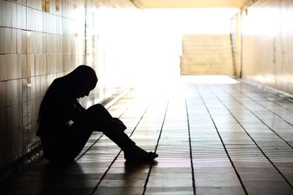 Depressed teenage girl sits in hallway in the dark