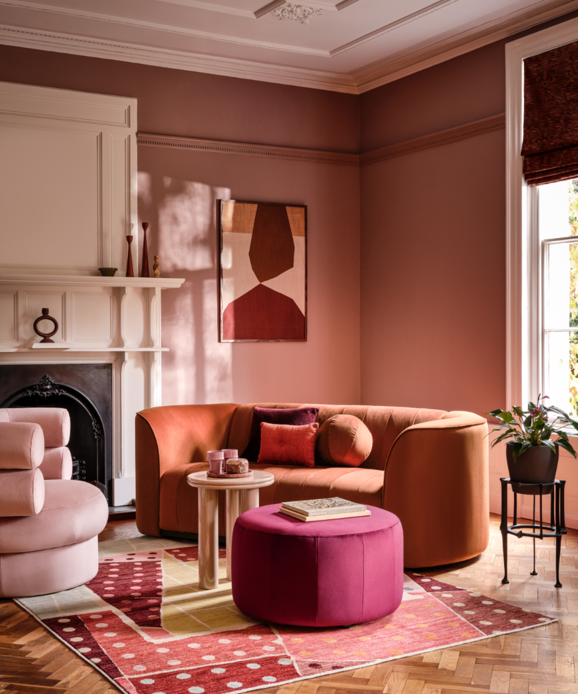 living room with curved orange sofa, dusky pink walls, pale pink fireplace and ceiling, bright pink pouffe
