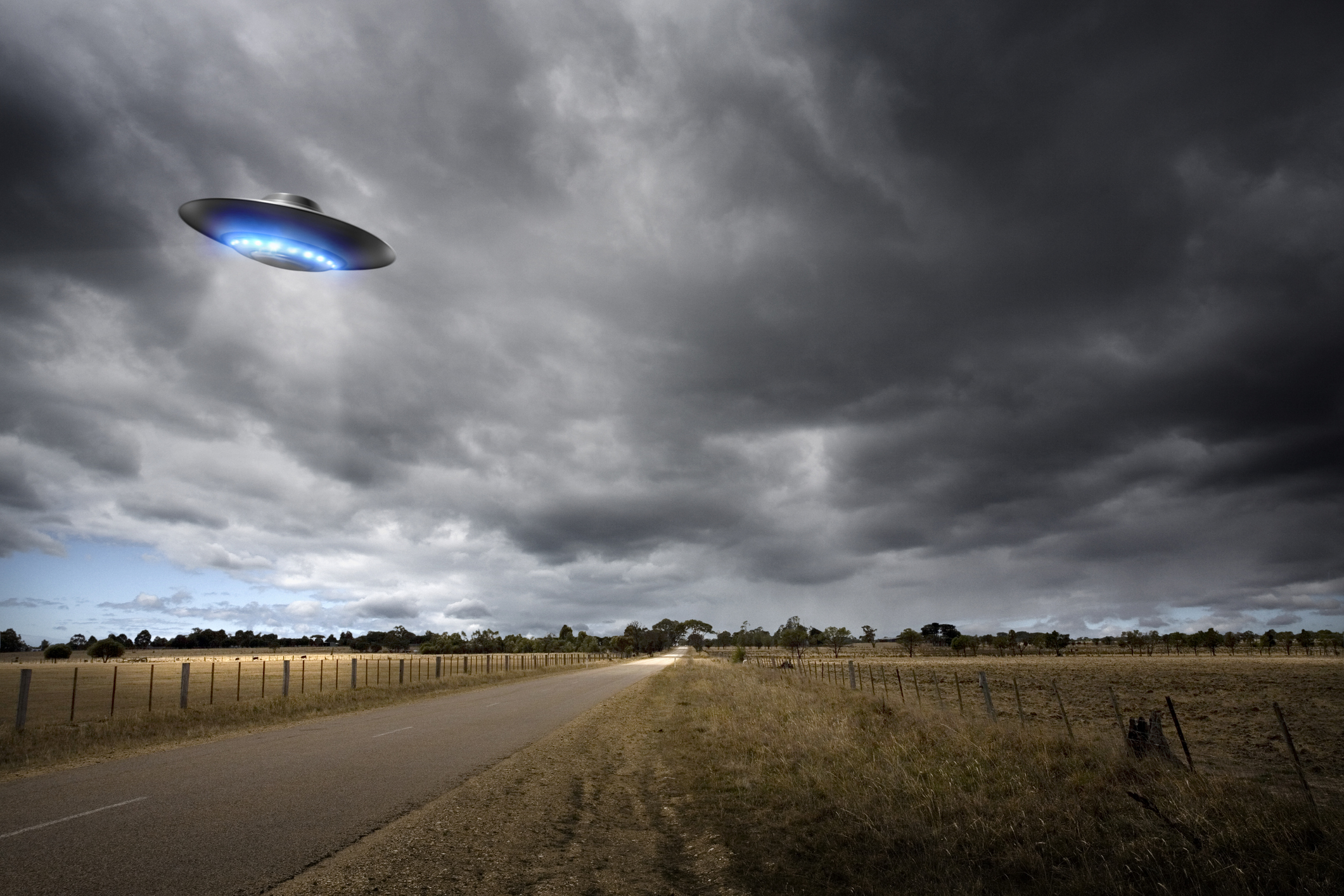 An illustration of a UFO hovering over a grassy field and road.