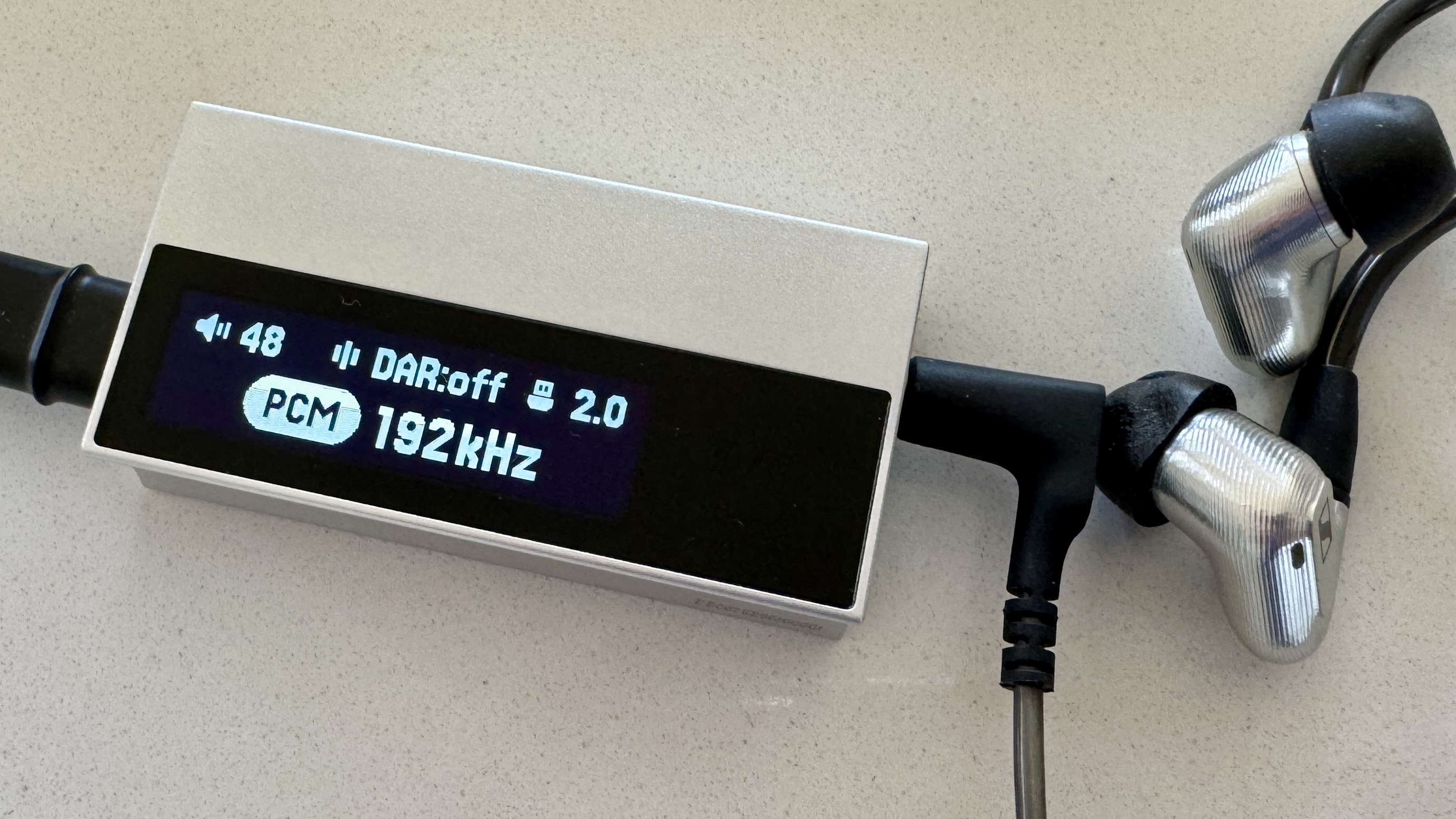 The Astell & Kern AK HC5 on a grey table, with the top plate illuminated and hooked up to Sennheiser IEMs and a FiiO digital audio player