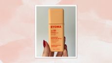 Image of hand holding Byoma Ultralight Face Fluid SPF50 on a pink watercolour background