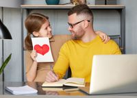 Daughter gives Father's Day card to father on Father's Day while he works on laptop computer,