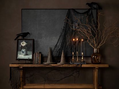 An entryway painted brown with a wooden console table and Halloween decorations including twig foliage, wicker witch hats, and taper candles