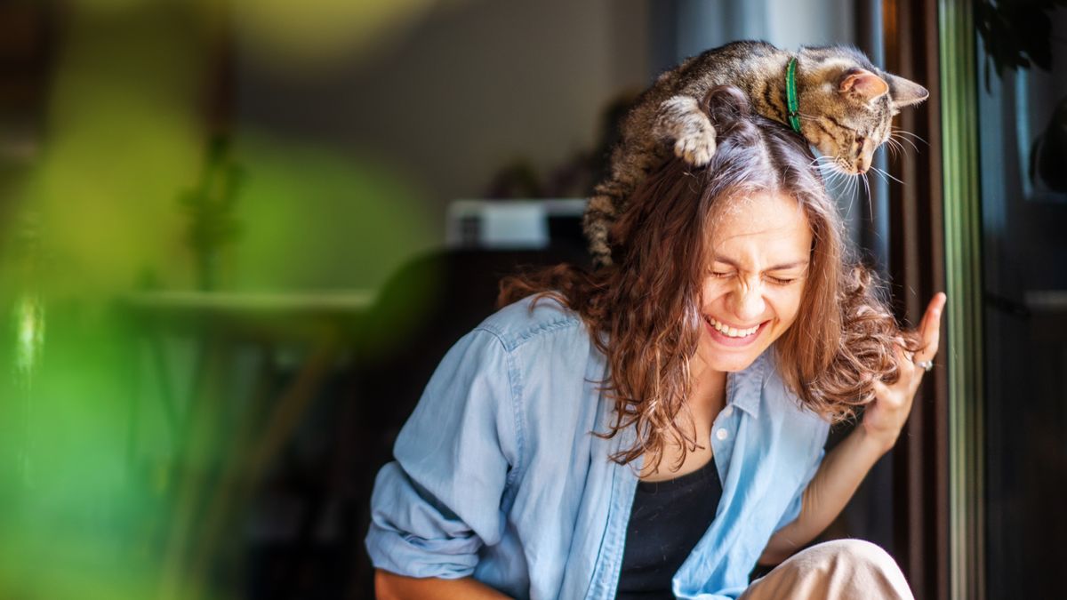 Woman laughing with cat on her head