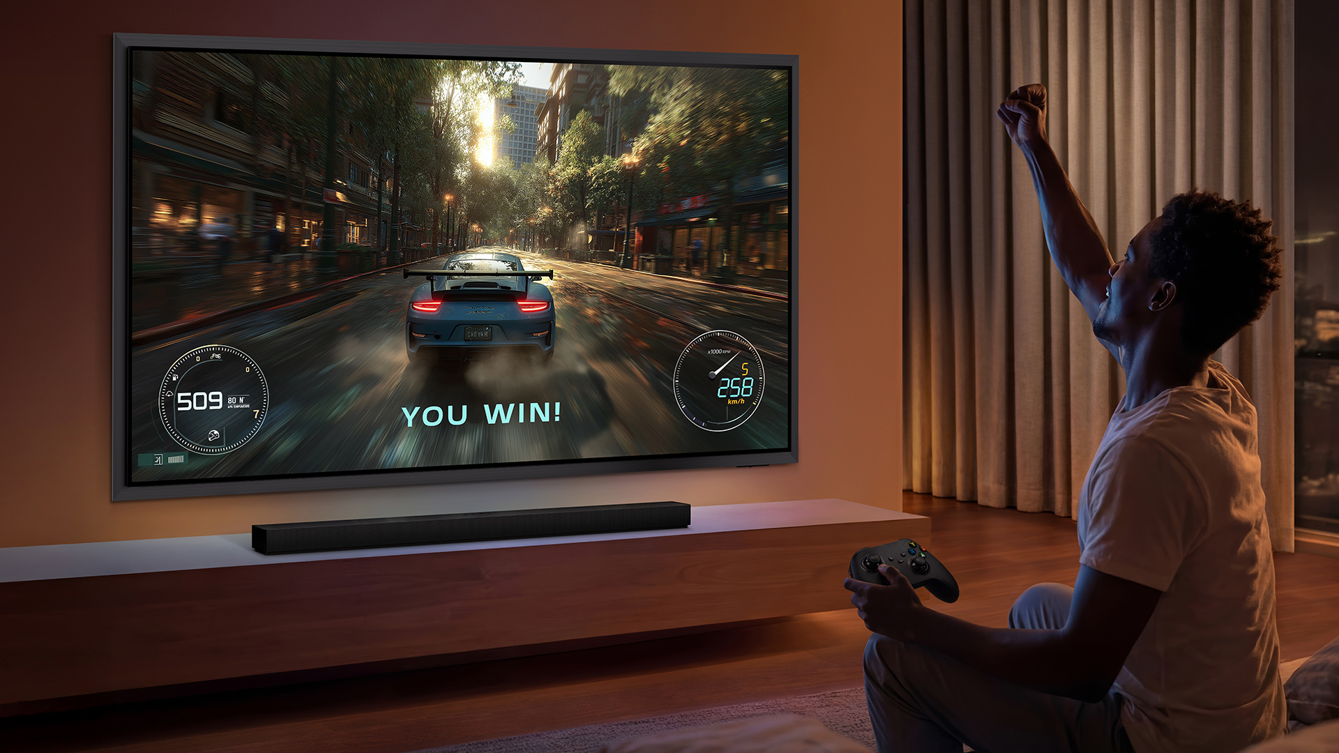 Samsung S99H 55-inch OLED TV in living room, man is gaming and celebrating win