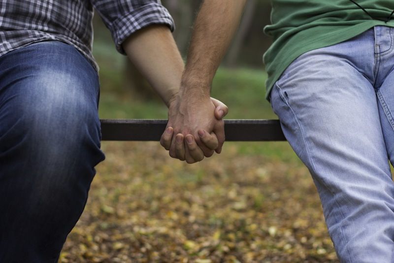 Two men hold hands, sitting on a bench