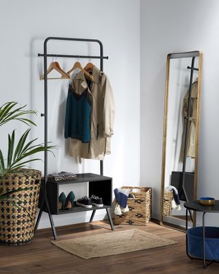 Clothes hanging off metal hanging rail on wooden coat hangers with houseplants and mirror