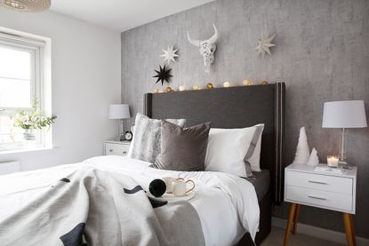 Bed with grey oversized headboard against concrete-effect wallpaper with white and oak modern bedside tables