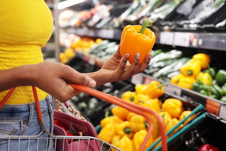 Woman putting bell pepper in supermarket basket