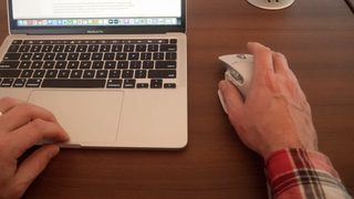 Hand moving mouse next to laptop on desk
