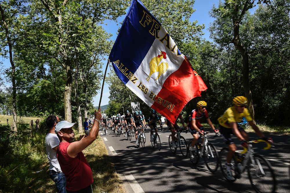 The peloton passes a spectator waving a French national flag reading 'Go France!' during the 190.5km 6th stage