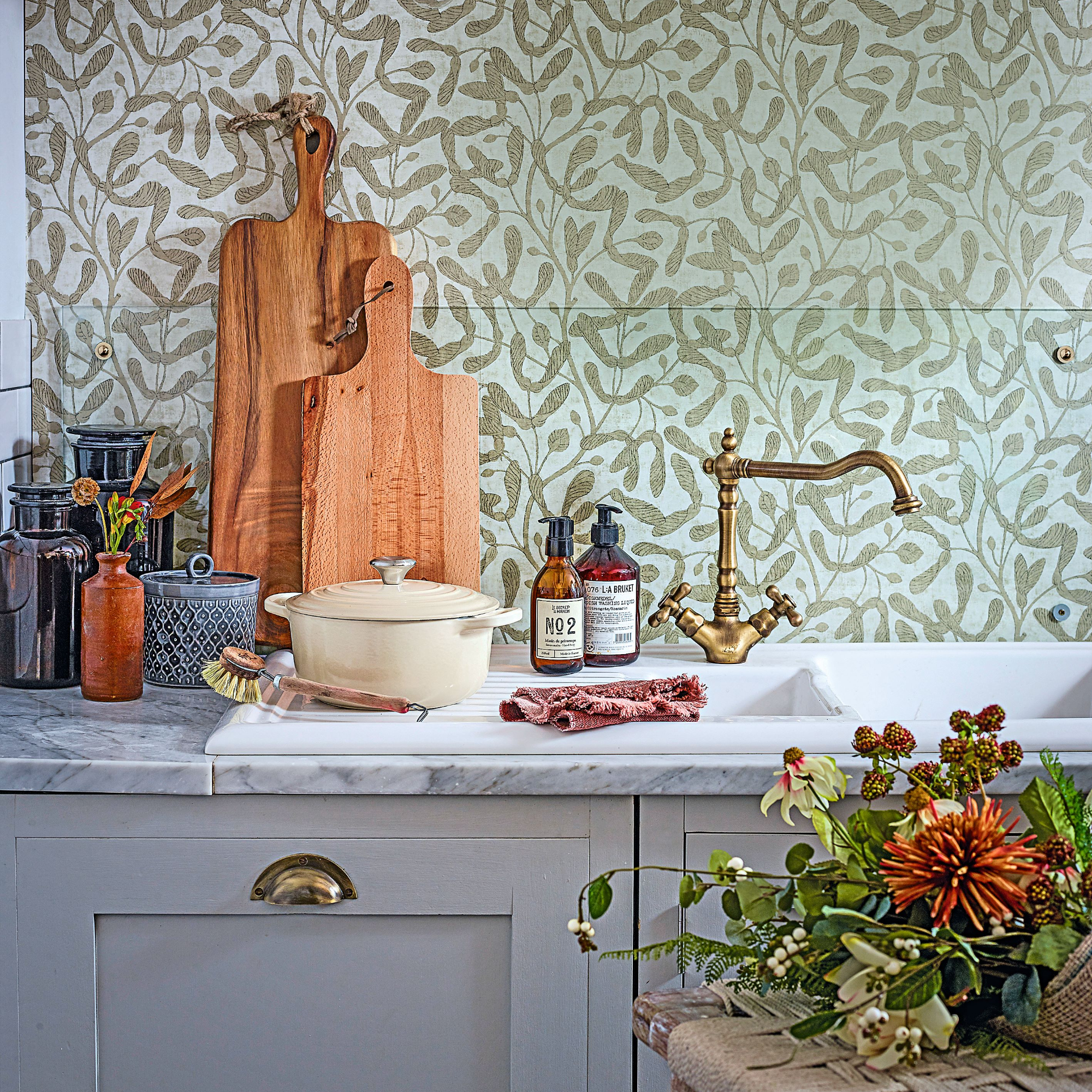 Kitchen sink and draining board in front of mistletoe wallpaper on a marble worktop with a stool decorated with flowers