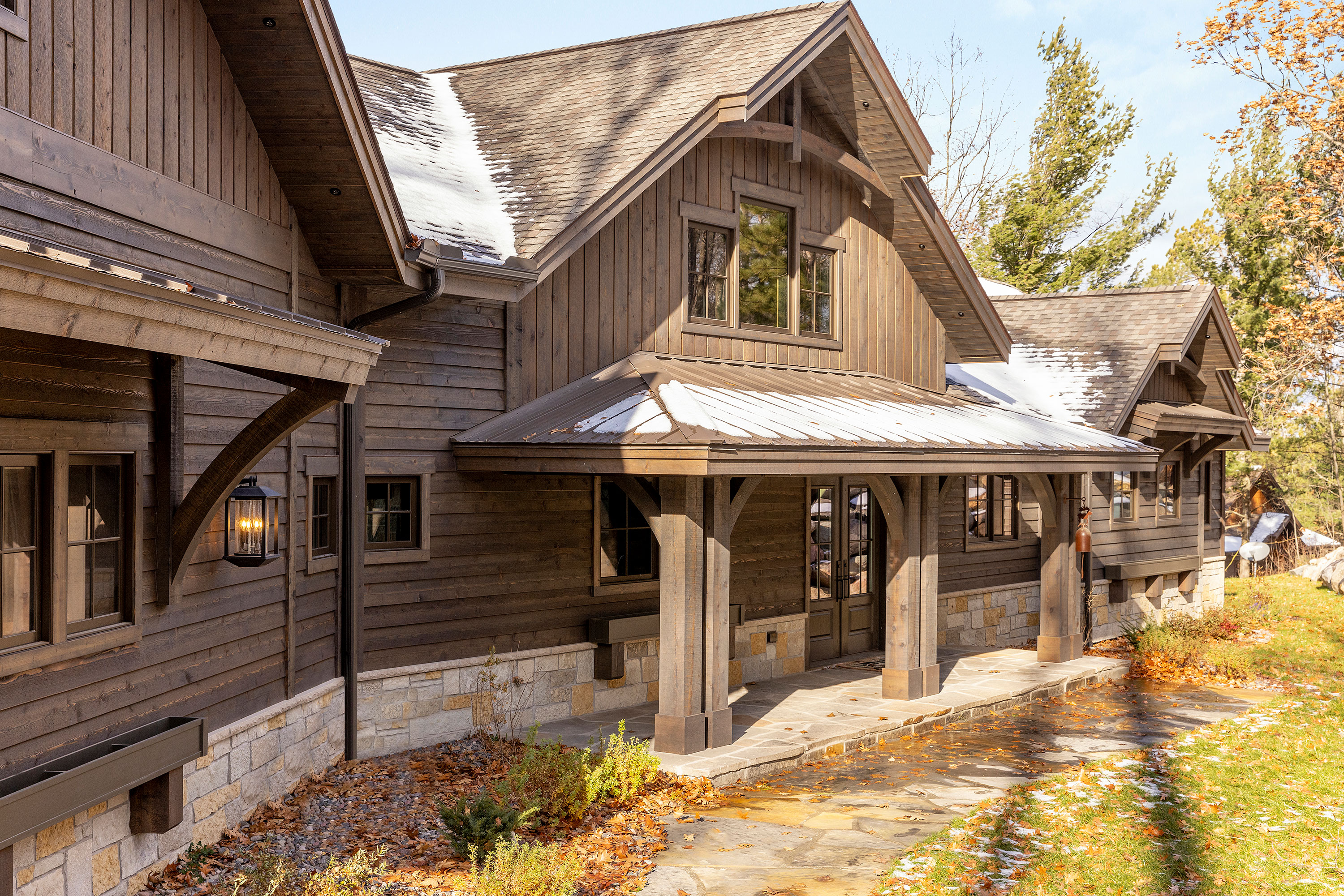 cabin home exterior in sunshine with snow on roof and bare trees