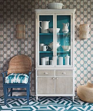 neutral glass fronted dresser in front of decorative wallpaper with pops of blue alongside an Orkney chair