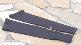 A pair of black Assos Evo 7 Arm warmers lie on a stone floor