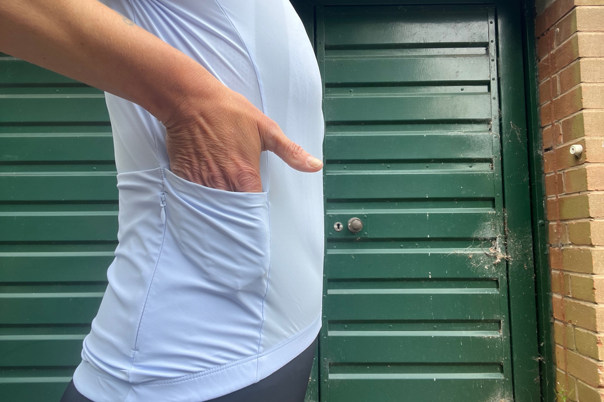 A hand enters the side pocket of the blue DHB Aeron Ultra Womens Short Sleeve Jersey