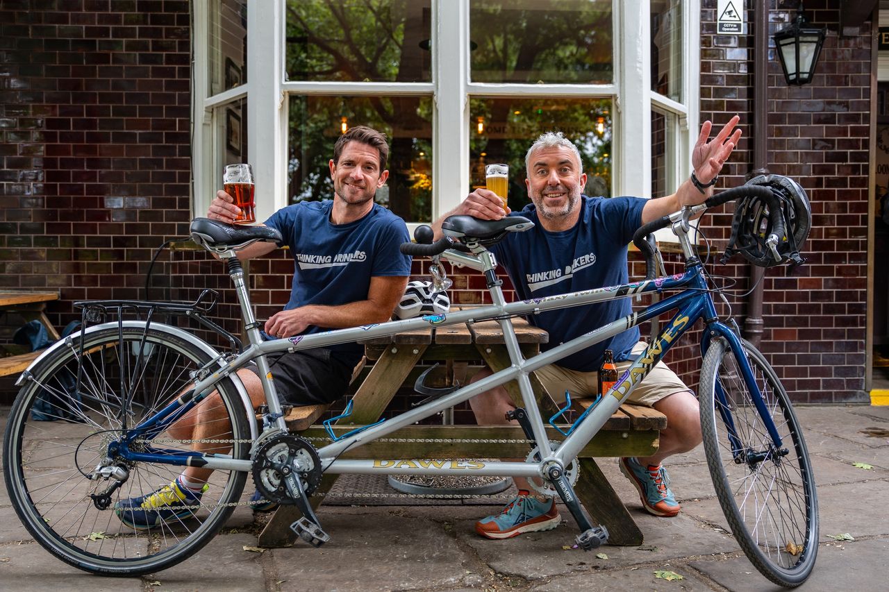 Ben and Tom with their tandem, raising a glass outside a pub