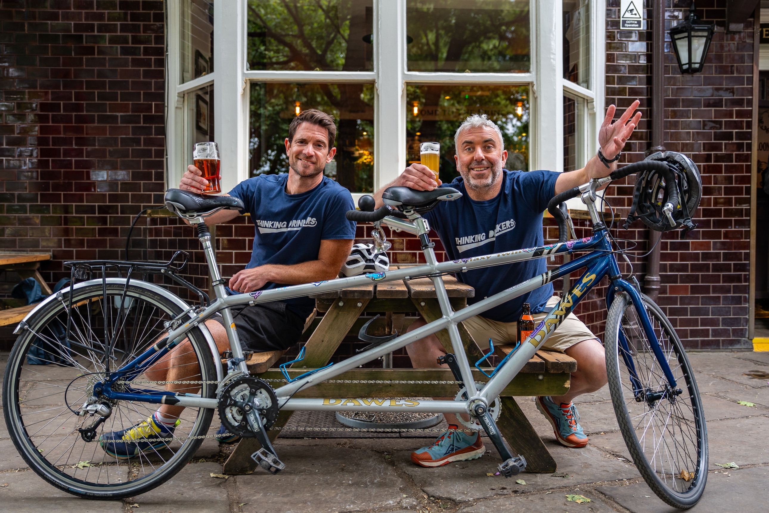 Tom and Ben with their tandem, raising a glass outside a pub