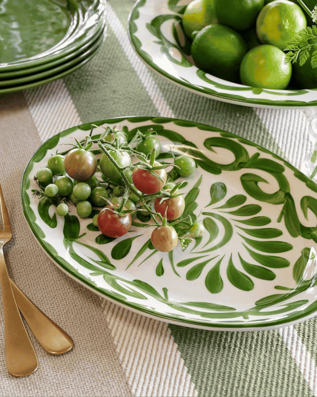 Puebla Porcelain Oval Serving Platter showcased in a rotating gif, placed atop a striped green and beige tablecloth and on a plain gray background.