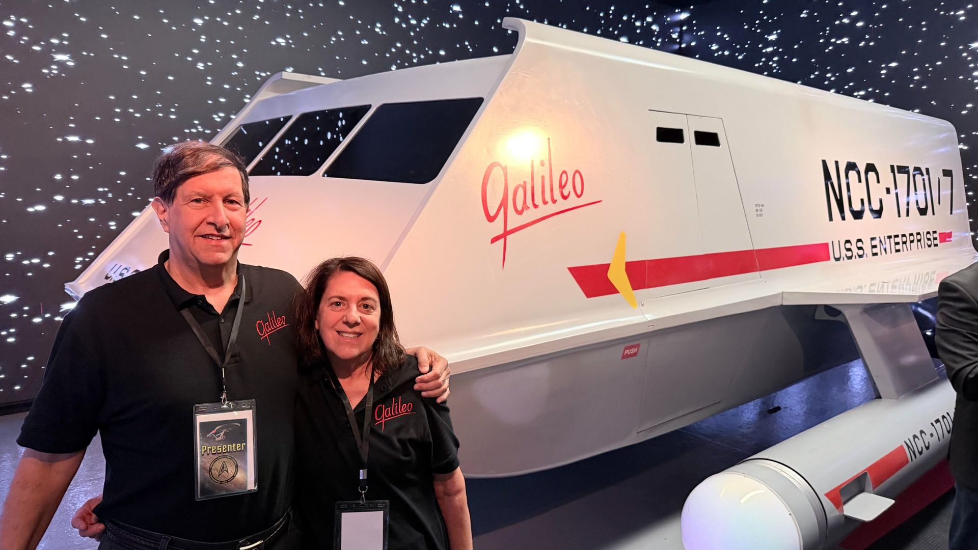 a man and his wife standing before a sci-fi shuttle mock-up