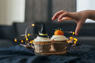 A child's hand trying to grab Halloween cupcakes with pumpkins on and a witch's hat.