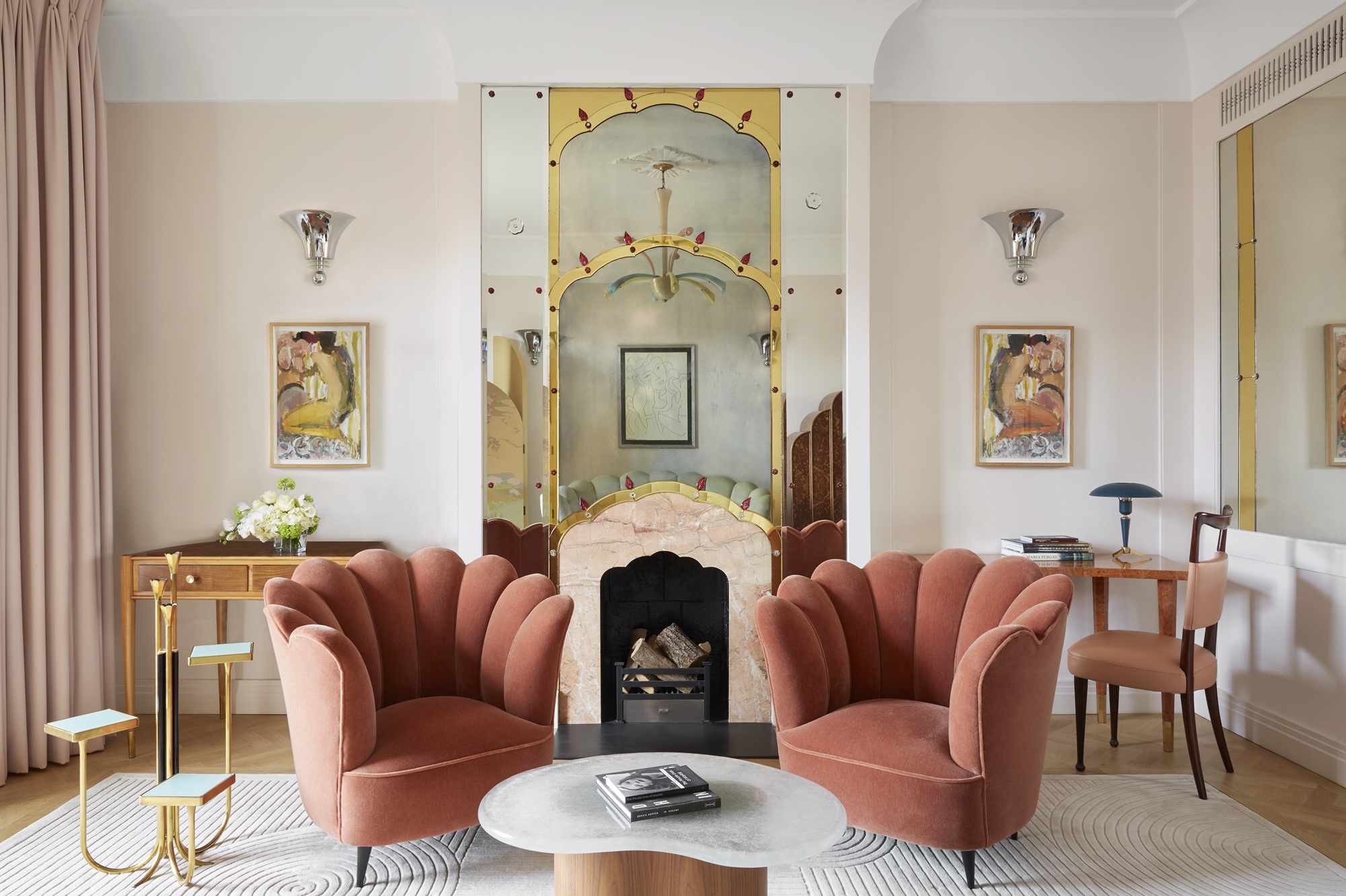 a hotel sitting room with art deco style, including scalloped pink chairs, and a decorative mirror on the fireplace