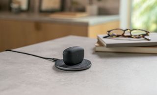 The Sony WF-1000XM5 in black wirelessly charging on a table.