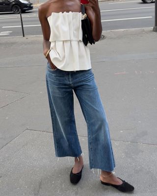 Sylvie wears white tube top with ruffles, cropped wide cut denim, and flat black mules.