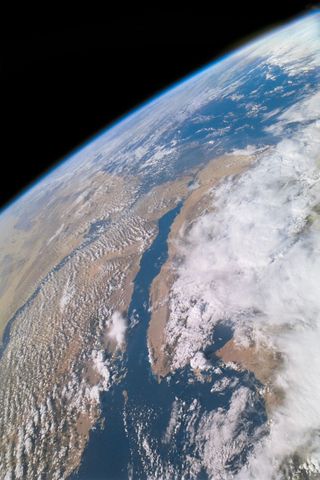 Earth from space, large white clouds shroud a blue sea and dark brown land.