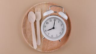 Image of a clock and wooden knife and fork sitting on wooden plate