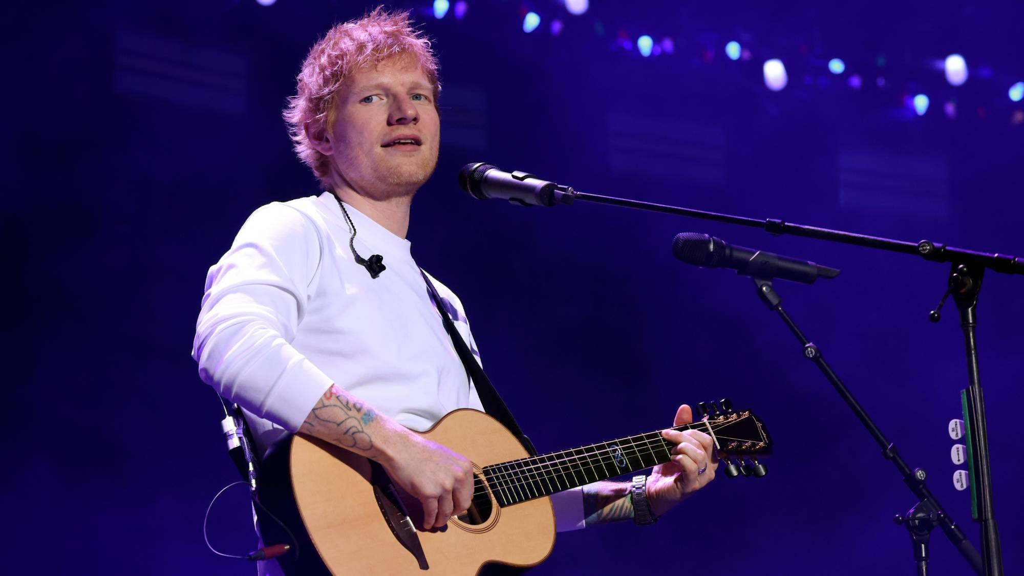 Ed Sheeran playing an acoustic guitar at a microphone