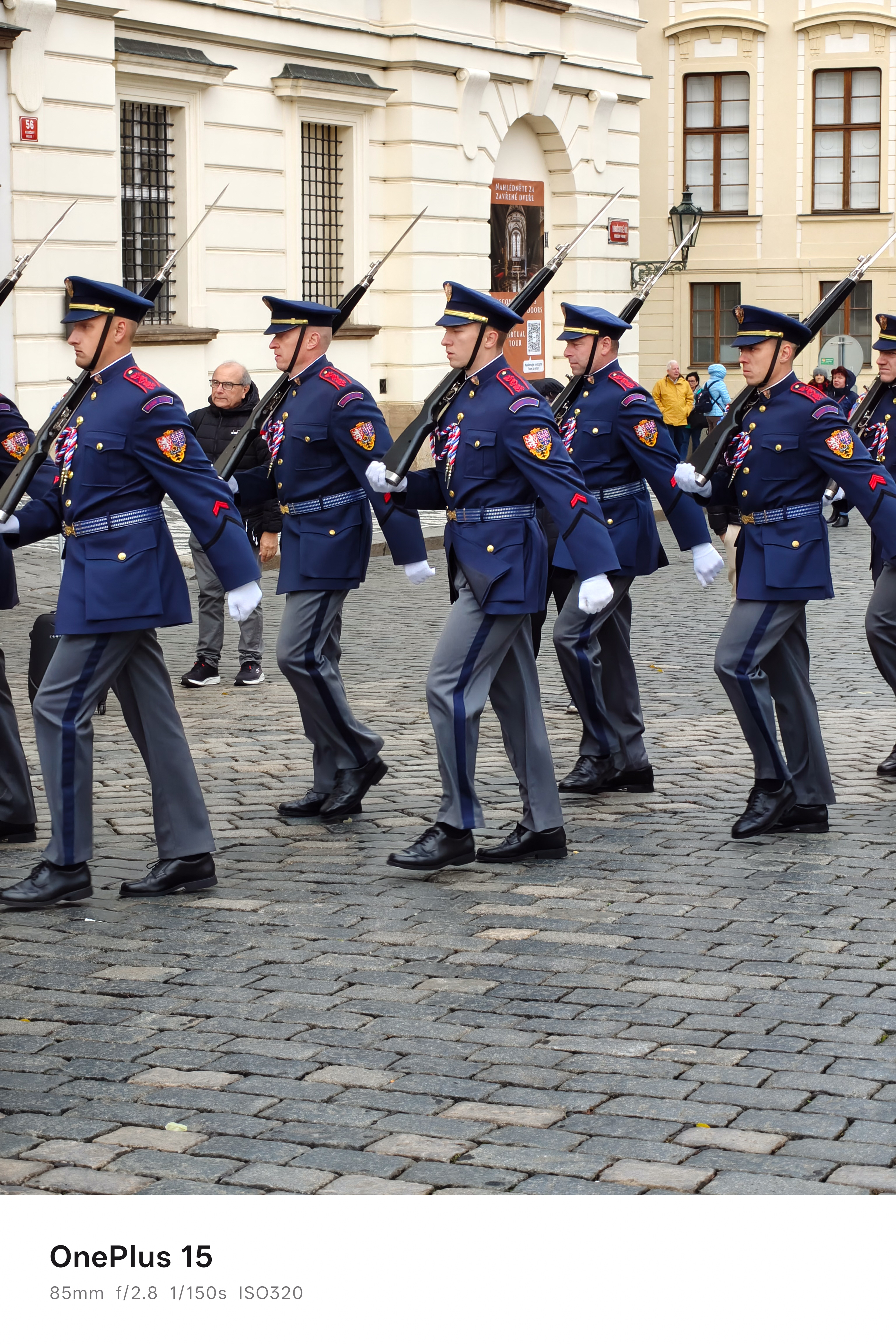 Soldiers in blue uniforms and carrying guns marching across a cobbled square
