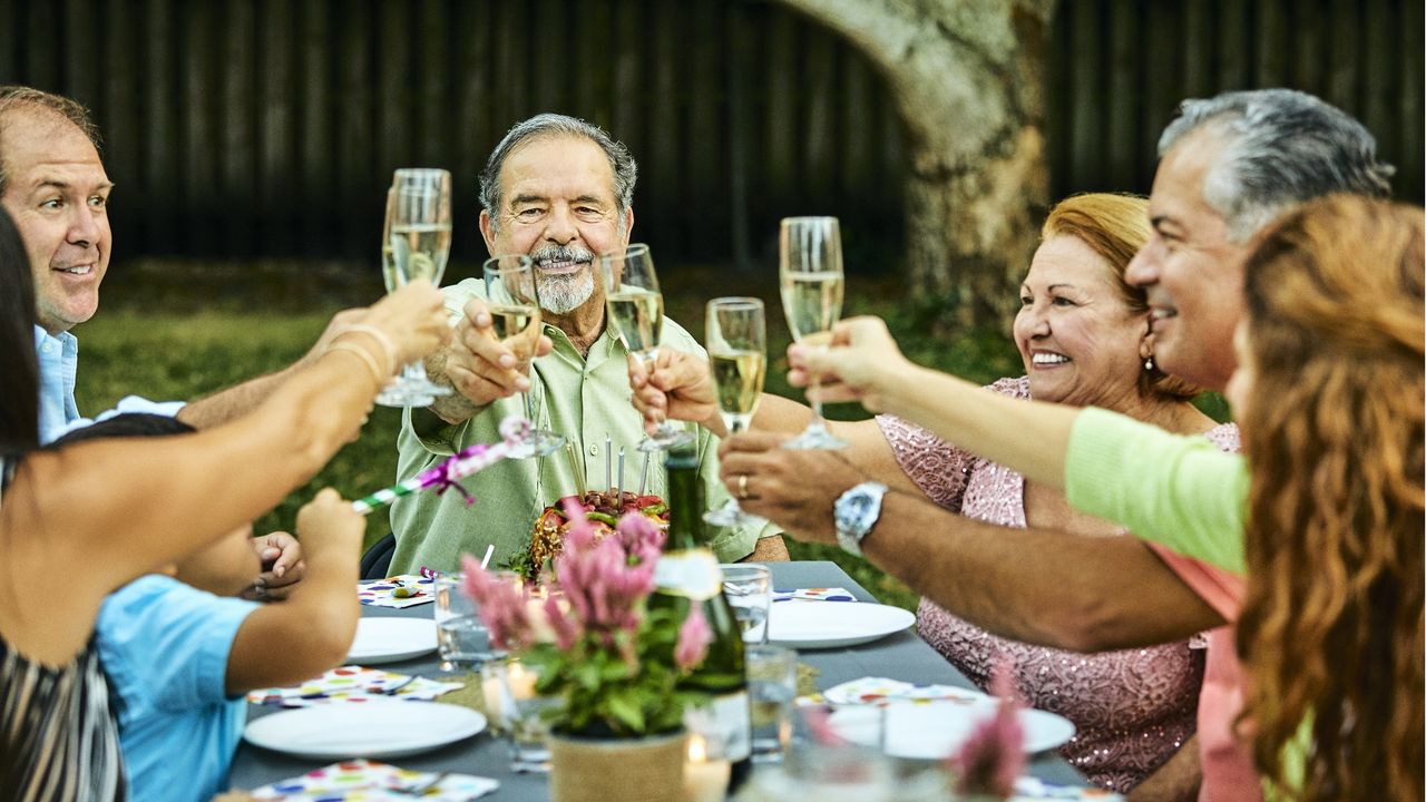 An extended family smile and laugh as they make a toast during dinner.