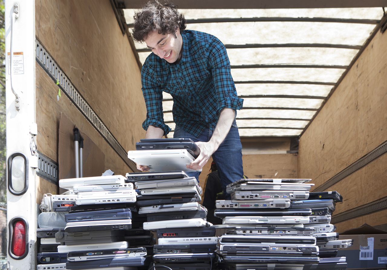 A man loading a pile of used laptops into the back of a van