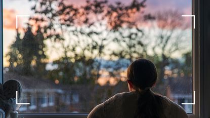 Woman looking out of the window into the sunset, to symbolise the price of loneliness