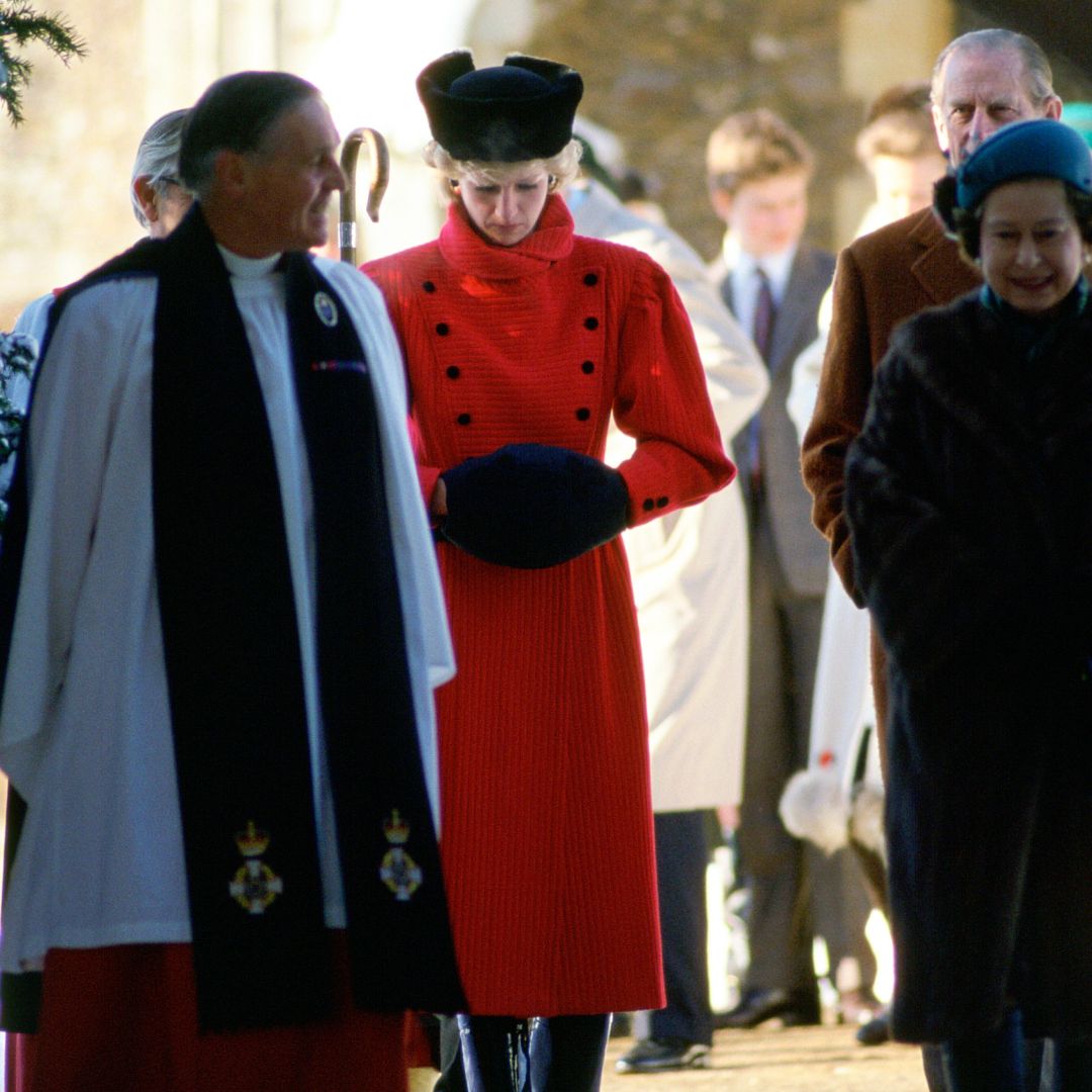 Princess Diana wearing a red coat and black hat looking sad walking next to Queen Elizabeth