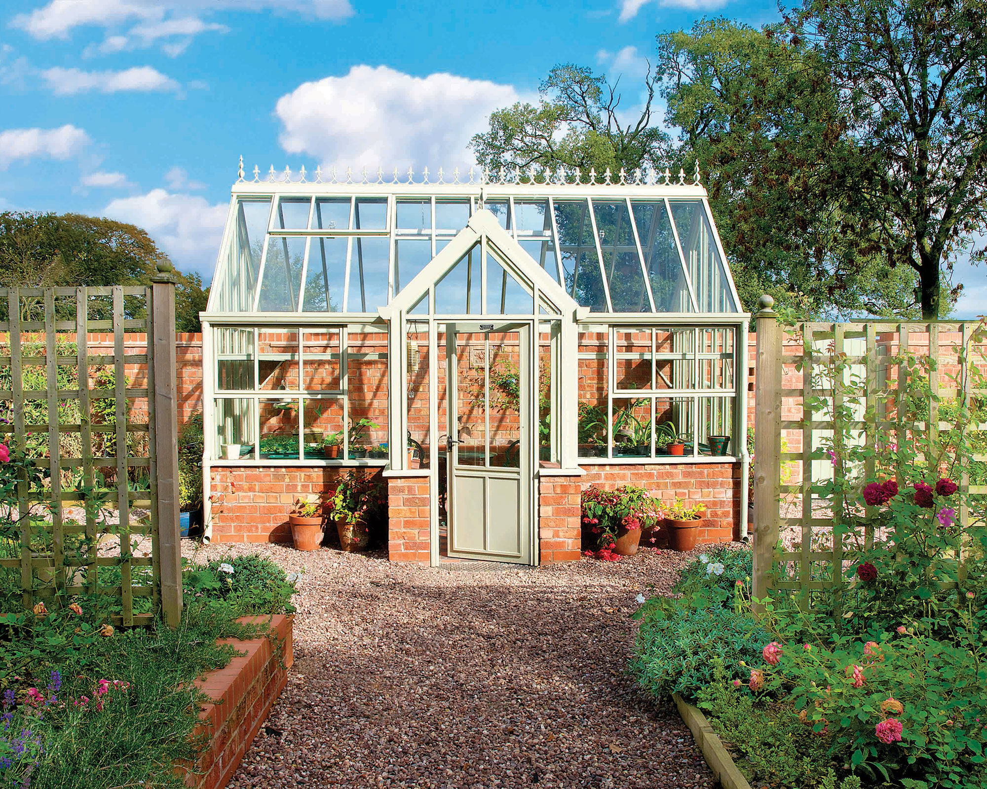 Cream and glass greenhouse, gravel path, climber fences, pink flowers and plants