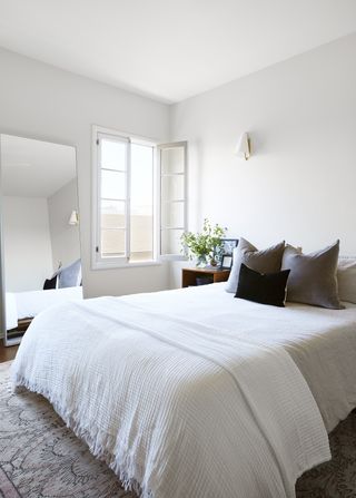 A white and cream bedroom scheme with an open window and large floor mirror.