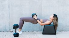 A woman performing a glute bridge with dumbbells