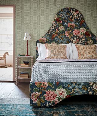 An oversize floral fabric upholstered bed and geometric print wallpaper in a cozy scheme.