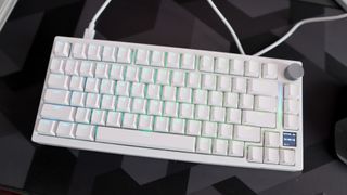 A Gamakay TK75HE gaming keyboard in white on a black and grey mouse pad with RGB lighting enabled.