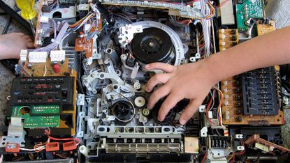 A close up of a series of electronic circuit boards and wiring, with a person's hand overtop.