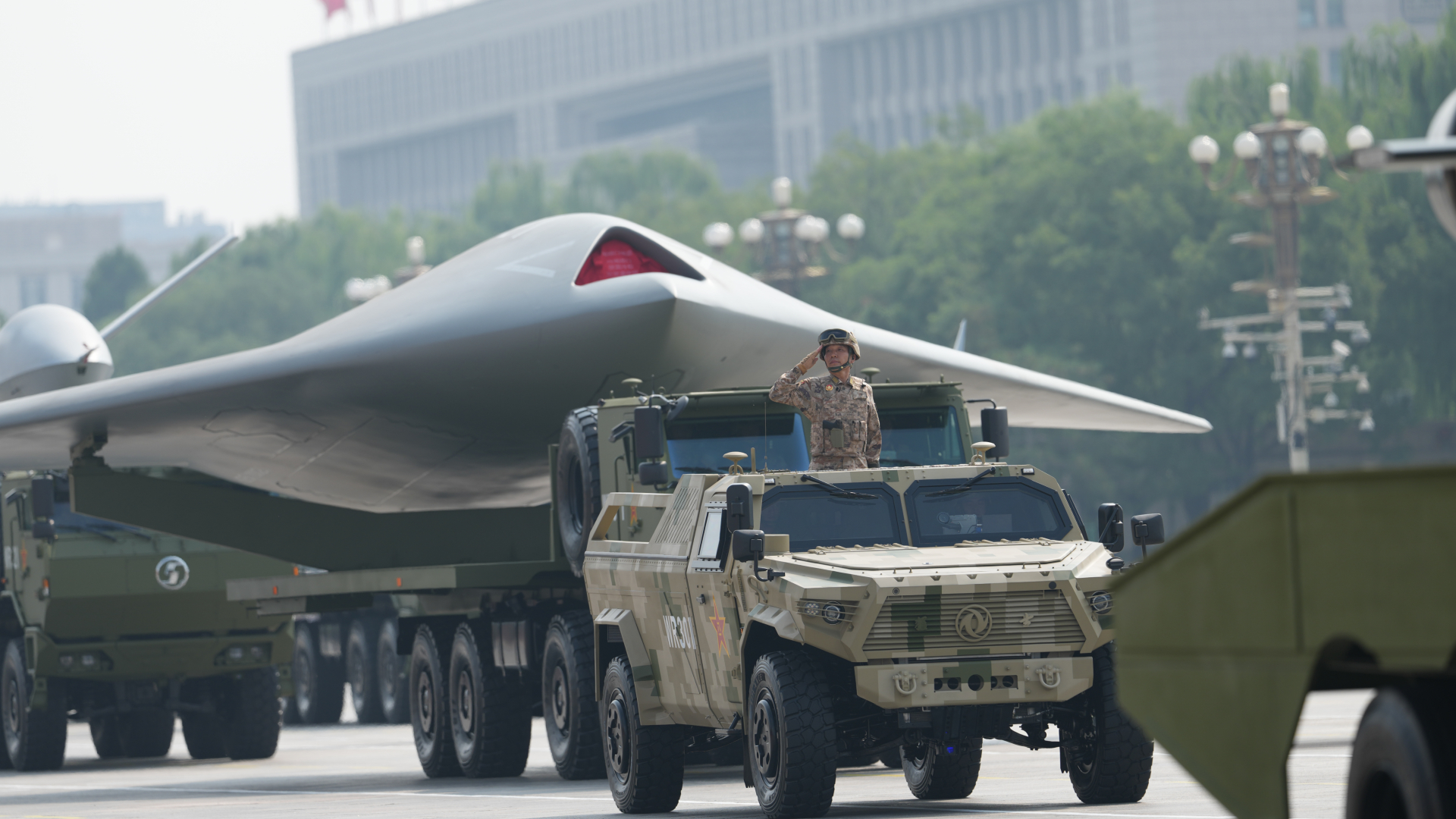 A large military truck rides in front of a giant military plane in the Chinese military parade