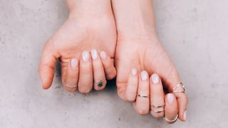 Woman hands with nude pink manicure and with many various silver rings on fingers on concrete gray background.