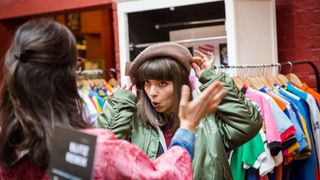 Woman tries on hat in shop, while friend looks on