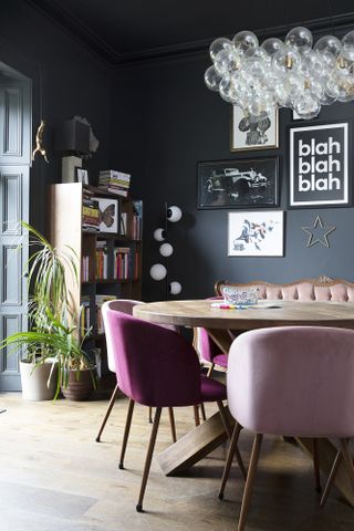 Black dining room with wooden table and pink dining chairs, and bubble chandelier above