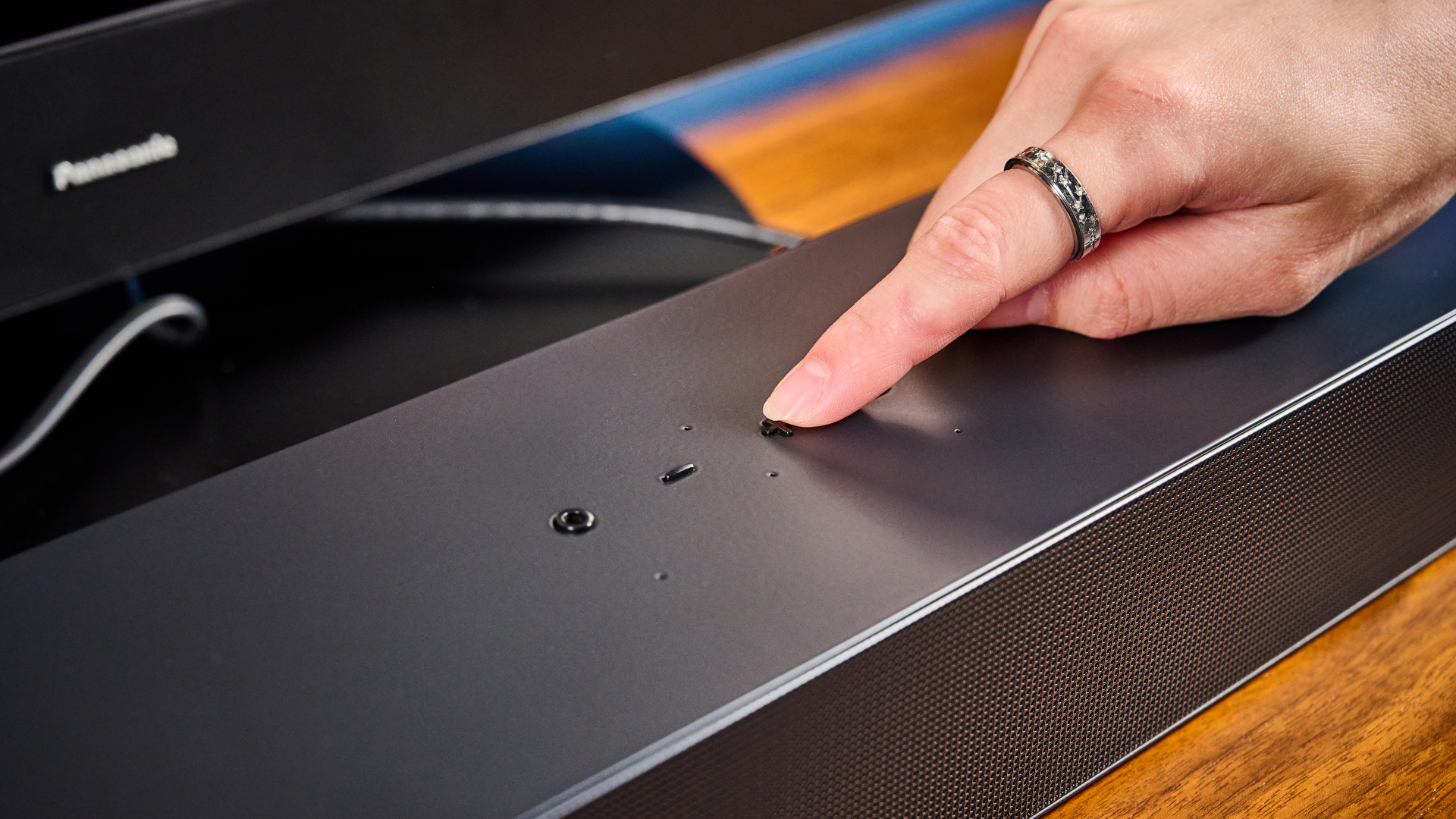 the samsung hw-s60D soundbar photographed on a wooden coffee table with a panasonic tv and a samsung soundbar against a blue background
