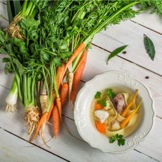 Carrots, celery root, and leeks next to a bowl of vegetable noodle soup